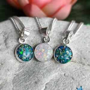 The Angelic Circle of Life DNA Pendant (8mm) features three pendants with colorful designs, set in a silver holder, displayed on a natural stone. Each pendant showcases vibrant, sparkling hues, ideal for a stylish accessory.