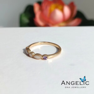 The Angelic Two Marquisette Three Genuine Birthstones DNA Ring features a gold band design with a central purple birthstone and marquisette accents, providing a unique and elegant appearance.