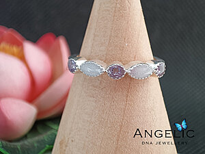 The Angelic Two Marquisette Three Genuine Birthstones DNA Ring features a silver band adorned with two marquise-shaped gemstones and one round gemstone, set in a unique pattern. The design includes three genuine birthstones.