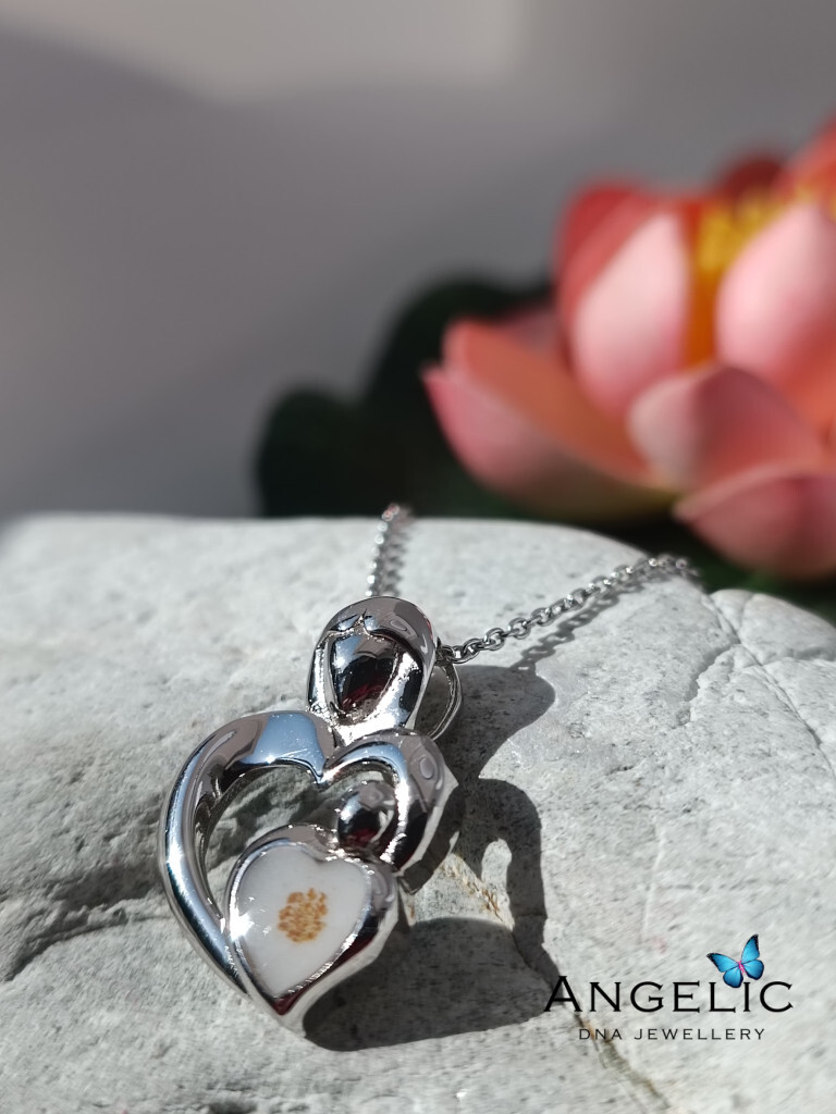 The Angelic An Grá DNA Pendant features a heart-shaped design in polished silver, showcasing a smaller heart with an embedded DNA element, suspended on a delicate silver chain.