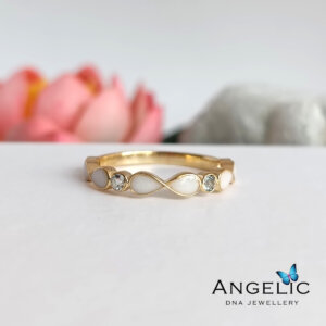 Elegant gold infinity ring featuring moonstone and sparkling accents, displayed with soft pink flowers in the background, showcasing a blend of sophistication and natural beauty. Perfect for special occasions or everyday wear.