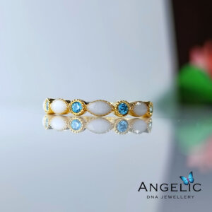 Gold ring featuring oval and round turquoise gemstones, elegantly designed with a polished finish, displayed on a reflective surface.