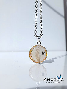 Silver chain necklace featuring a round pendant with a beige design and a black letter "R," reflecting the light and showcasing the craftsmanship of Angelic DNA Jewellery.
