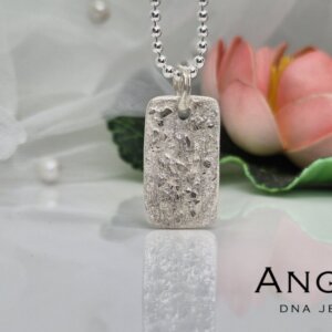 Silver pendant necklace with intricate floral design, showcased against a soft background with pearls and a flower. Angelic brand logo displayed.