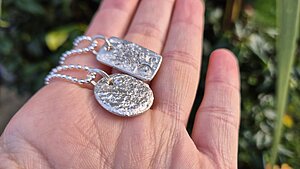 Hand holding two silver pendants, one rectangular and one circular, showcasing intricate designs and a polished finish, ideal for jewelry enthusiasts.